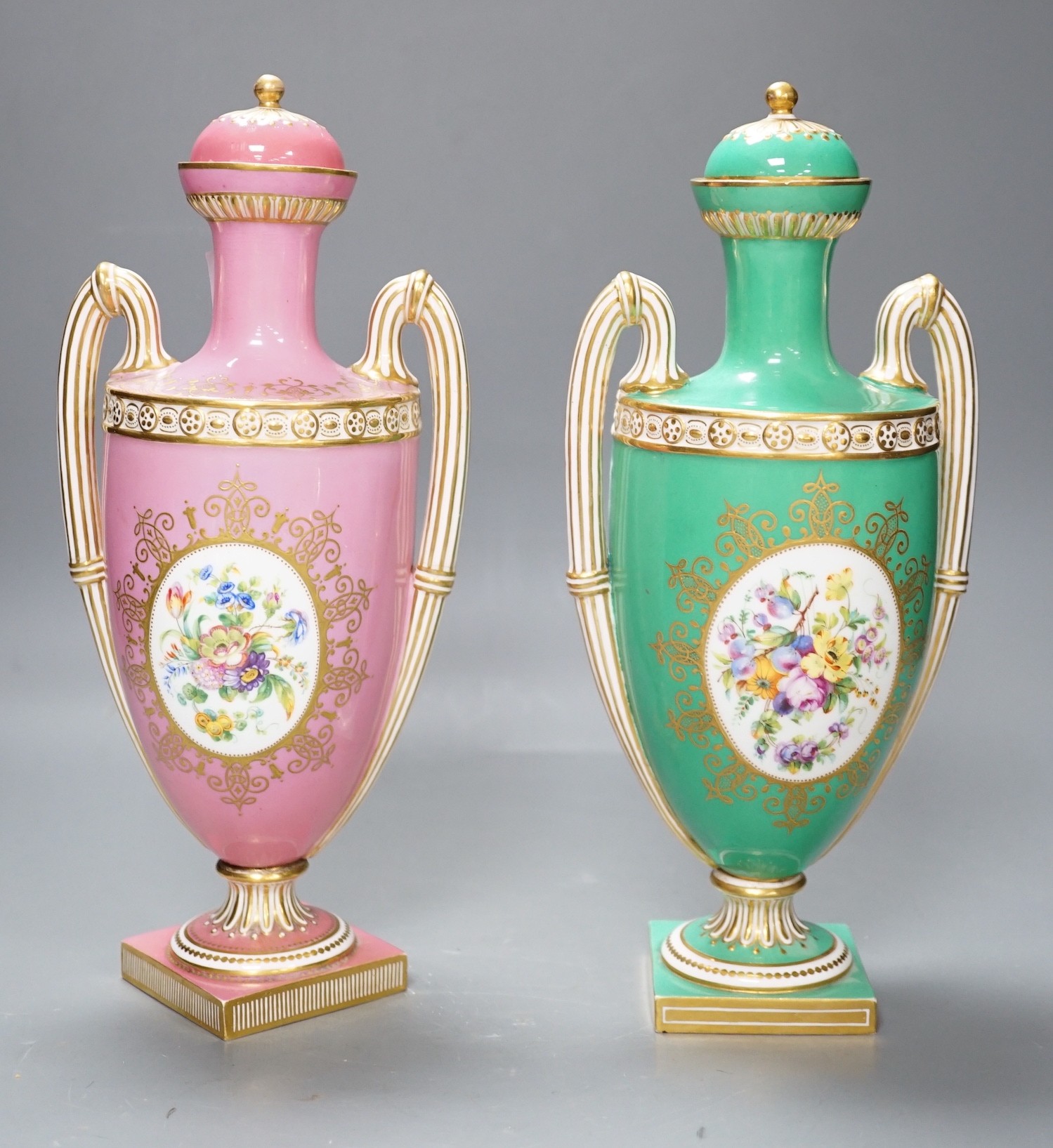 A pair of Coalport Coalbrookdale two handled vases with central oval panelled floral painting and gilt decoration, one green and the other pink, 29cm high